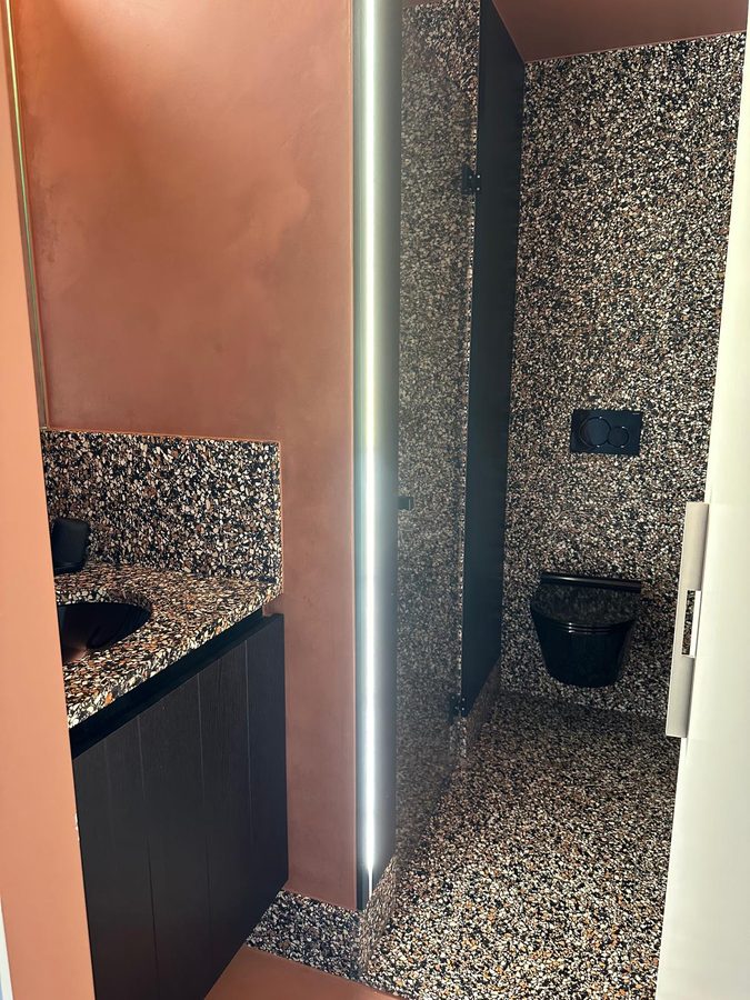 Toilet en wastafel in terrazzo met terracotta muren en verlichte spiegel
