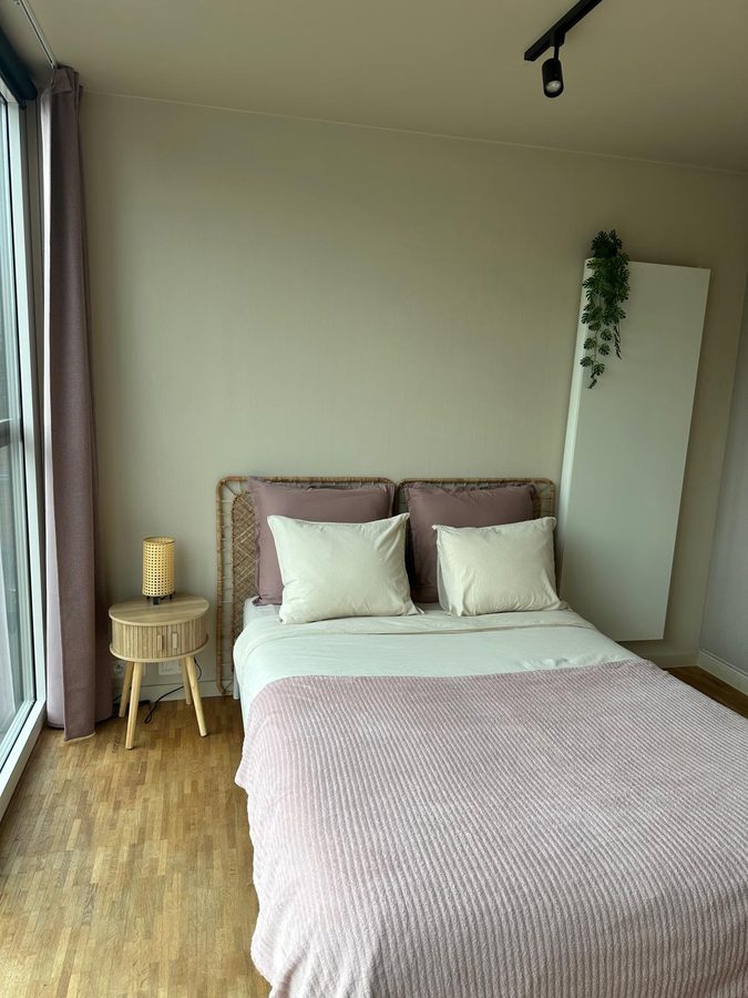 Bed met oudroze kussens, rieten hoofdeinde en rond nachtkastje