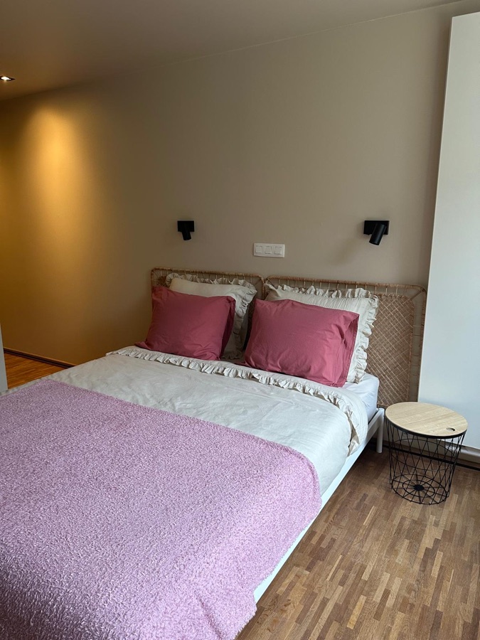 Bed met rieten hoofdeinde, roze plaid en rond bijzettafeltje